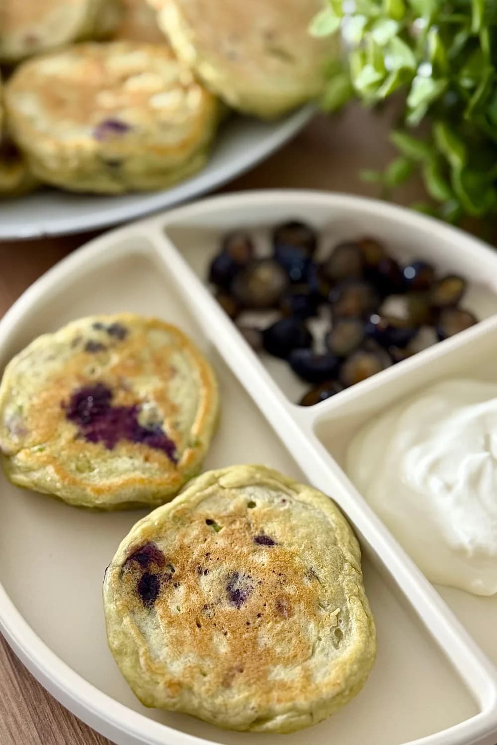 "Stack of homemade avocado blueberry pancakes on a white plate with fresh bananas and avocado in the background"
