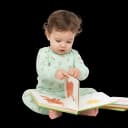 Cute baby or toddler sitting and turning pages of a board book, demonstrating early fine motor skills and literacy development.
