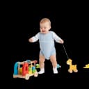 Happy baby or toddler walking and pulling a wooden giraffe pull toy, showing development of gross motor skills and coordination.