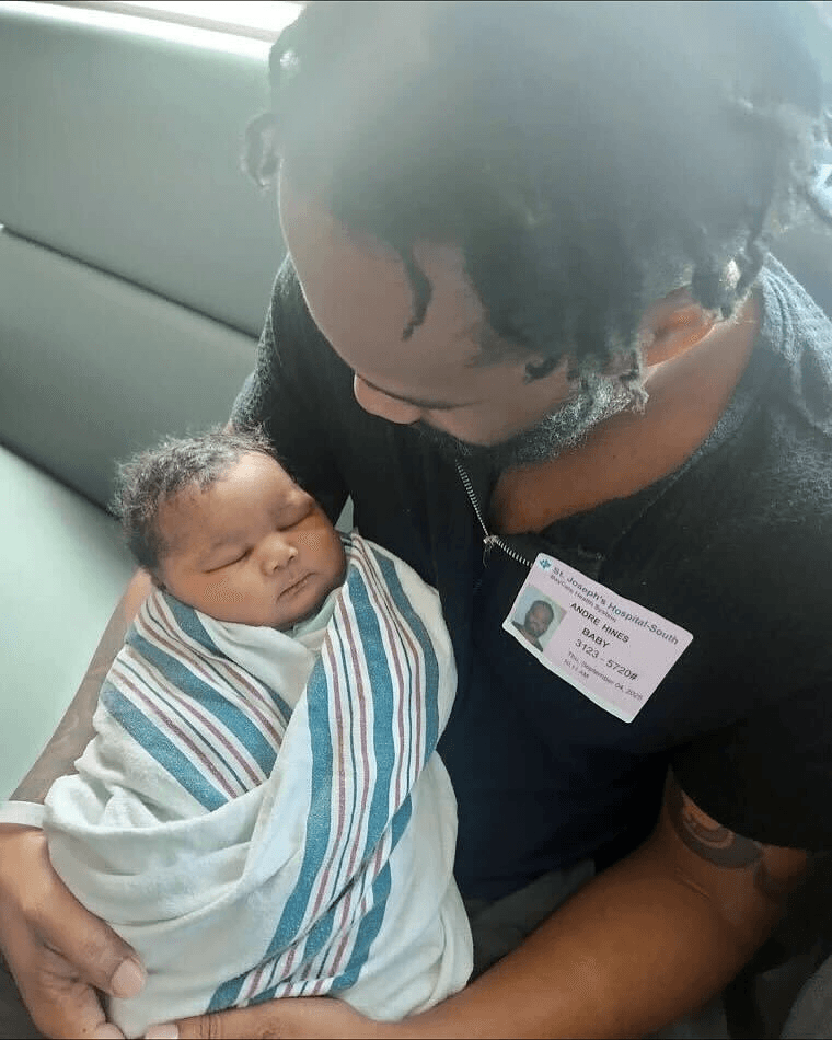 Man holding a newborn baby wrapped in a hospital blanket.