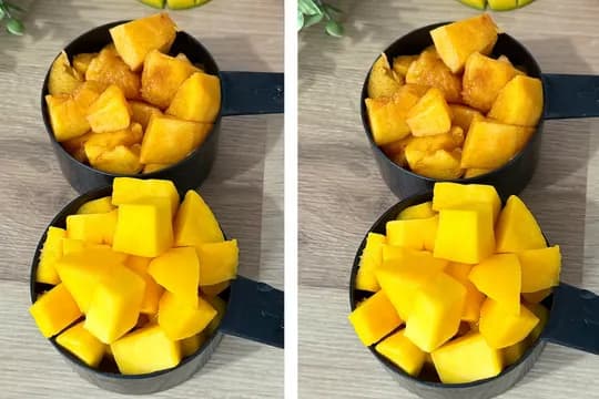 "Two measuring cups filled with fresh and frozen mango chunks on a wooden surface – ideal ingredients for homemade mango popsicles or smoothies."