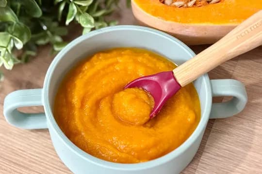 "Vibrant butternut squash baby food puree in a light blue bowl with a spoon, ready for feeding."