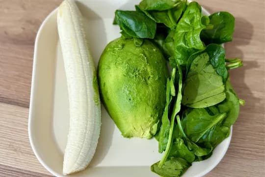 "Fresh banana, ripe avocado, and organic spinach on a plate – ingredients for a healthy green smoothie"