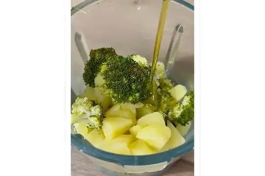 Blending steamed apple and broccoli with olive oil into a smooth baby purée.