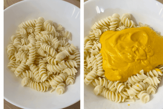"Cooked pasta in a large bowl being mixed thoroughly with creamy carrot sauce until evenly coated."