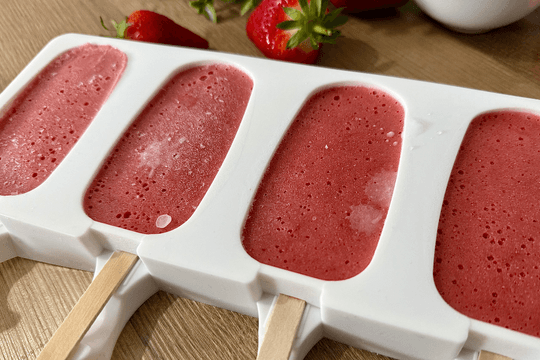 "Popsicle molds filled with strawberry yogurt blend, ready to be placed in the freezer."
