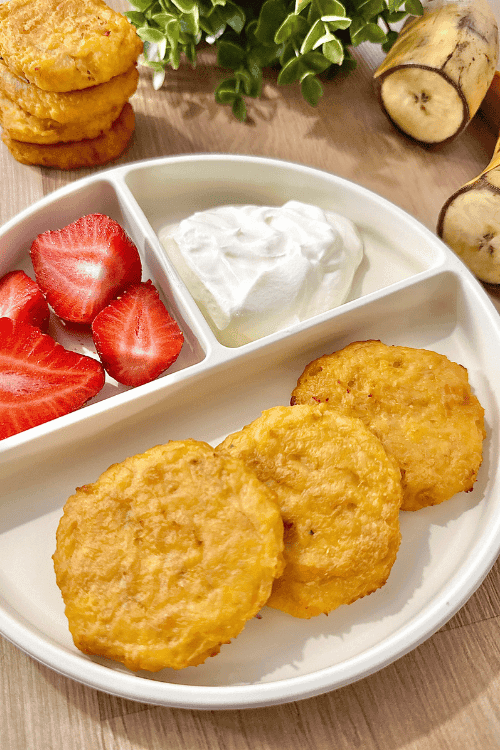 Plate of baked cheesy plantain fritters served with fresh strawberry halves and a dollop of yogurt on a divided white dish.