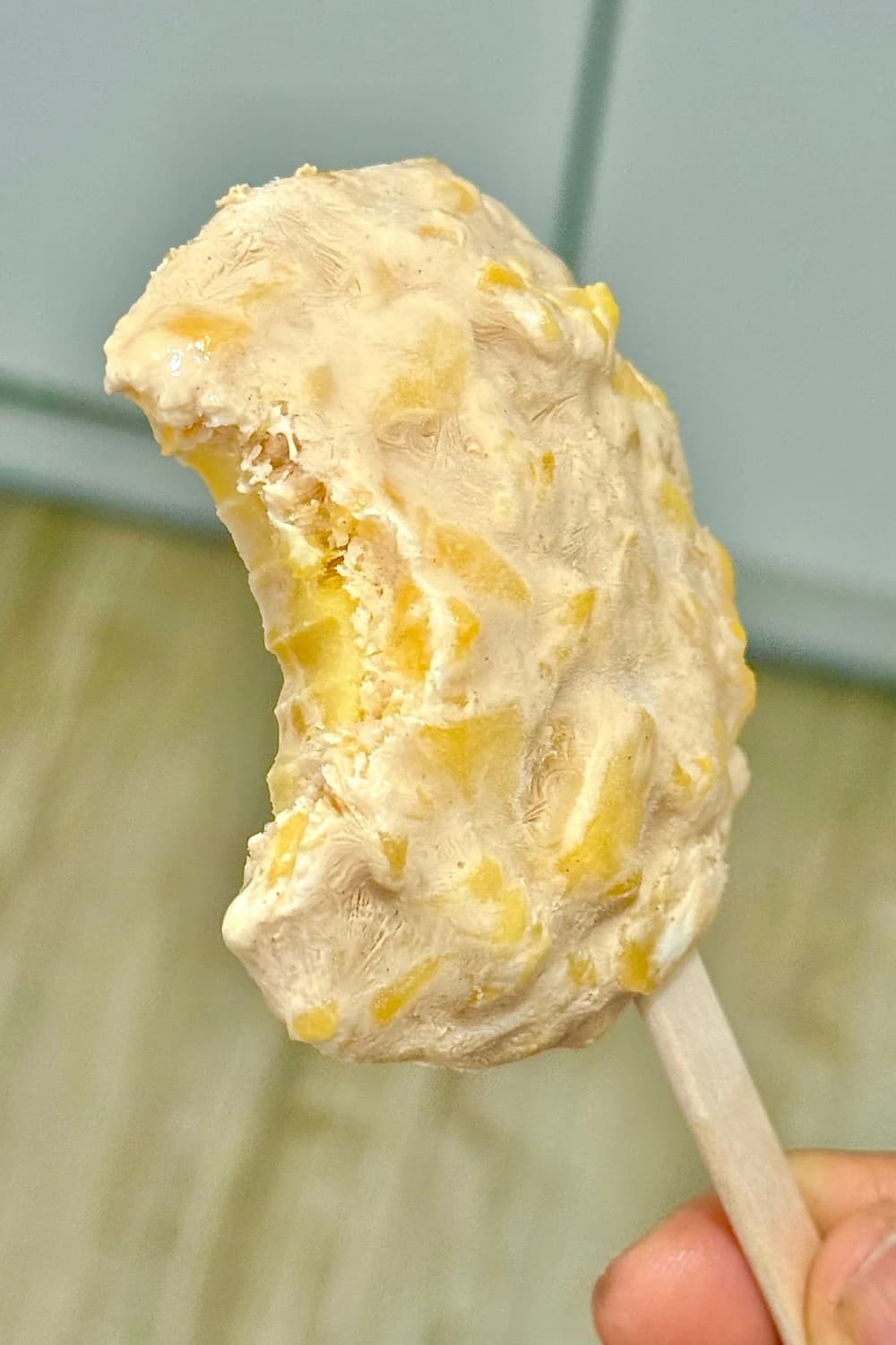 "Close-up of a bitten homemade mango yogurt popsicle, showing creamy texture and visible mango chunks. A refreshing and healthy frozen treat."