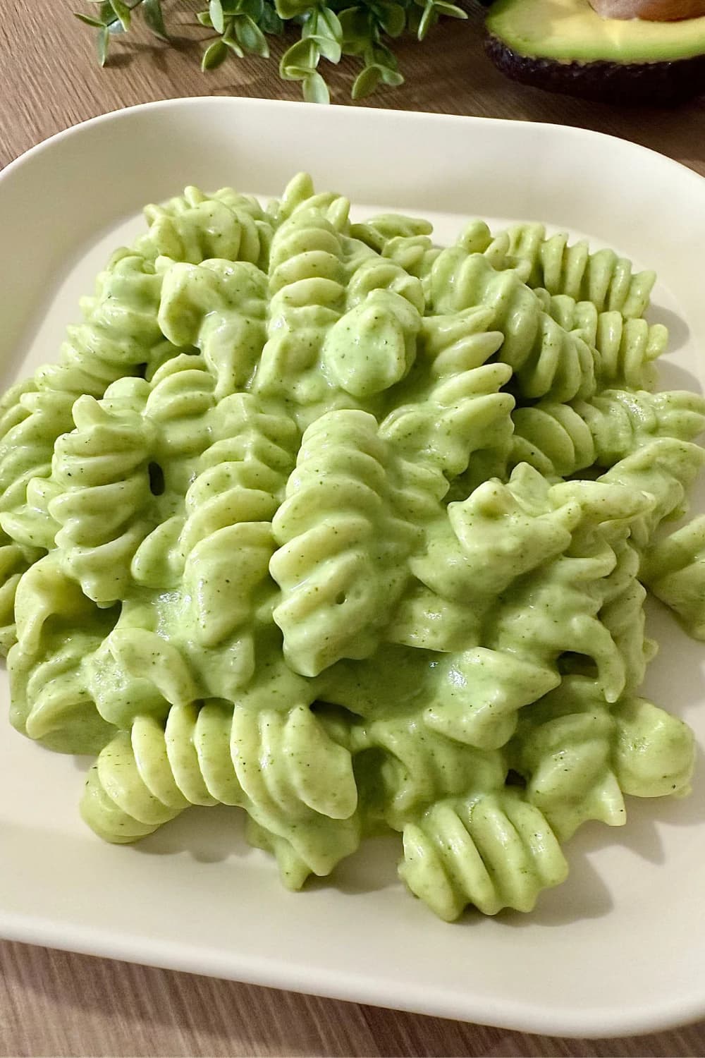 "Creamy avocado and broccoli pasta with rotini noodles on a white plate, vegan and dairy-free healthy meal"