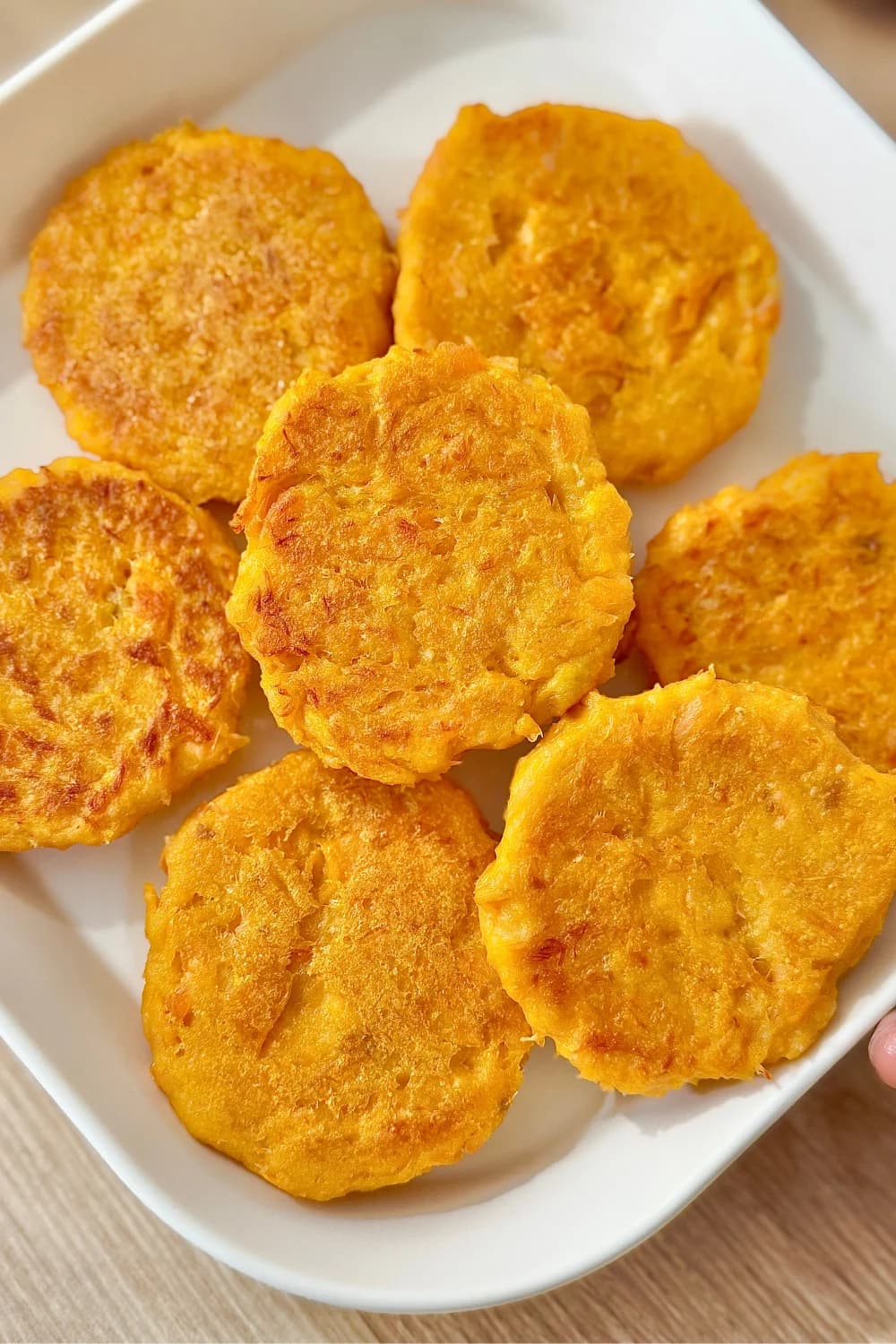 A close-up, top-down view of a white rectangular dish filled with several golden-brown salmon and sweet potato fritters.