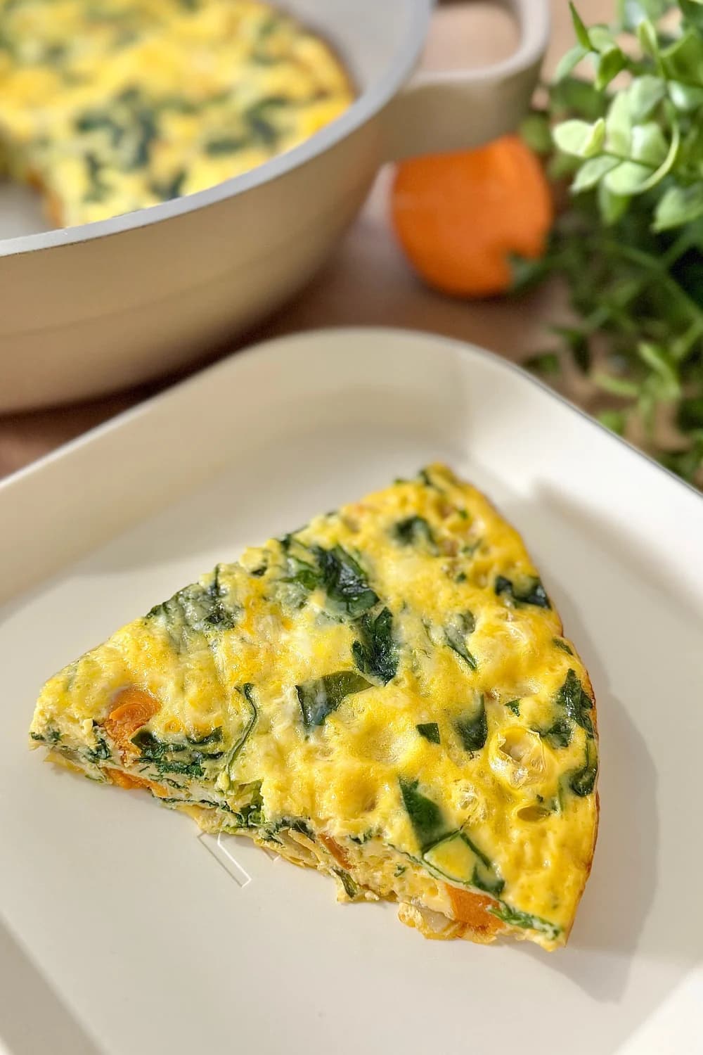 A vibrant slice of potato frittata rests on a white, rectangular plate.