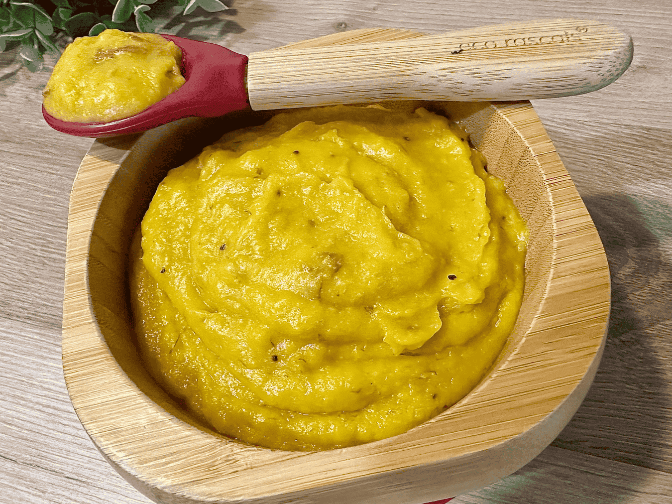 A smooth, vibrant orange purée made from steamed carrots and ripe plantains, served in a baby bowl with a small spoon, perfect for homemade baby food.