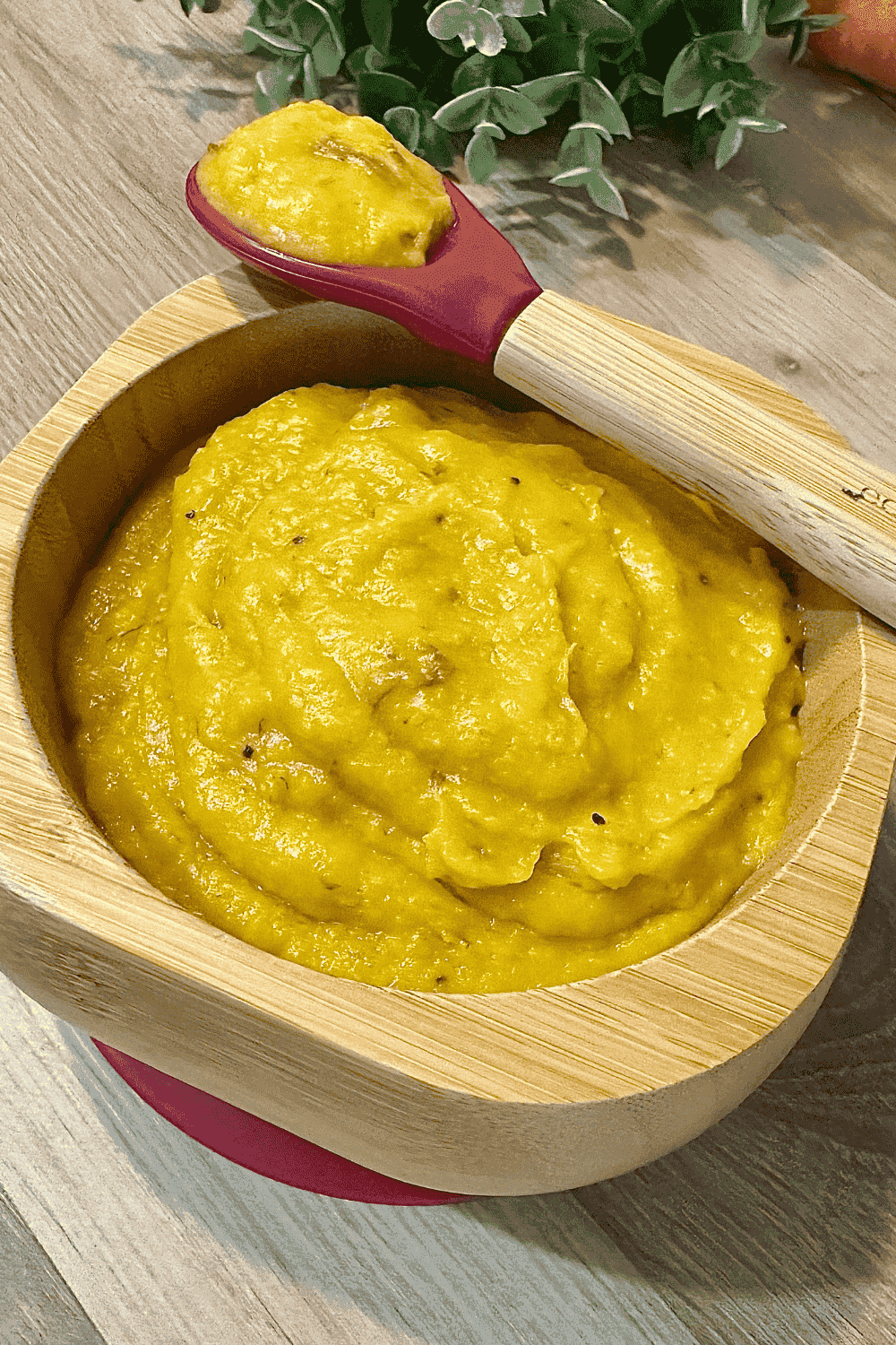 A smooth, vibrant orange purée made from steamed carrots and ripe plantains, served in a baby bowl with a small spoon, perfect for homemade baby food.