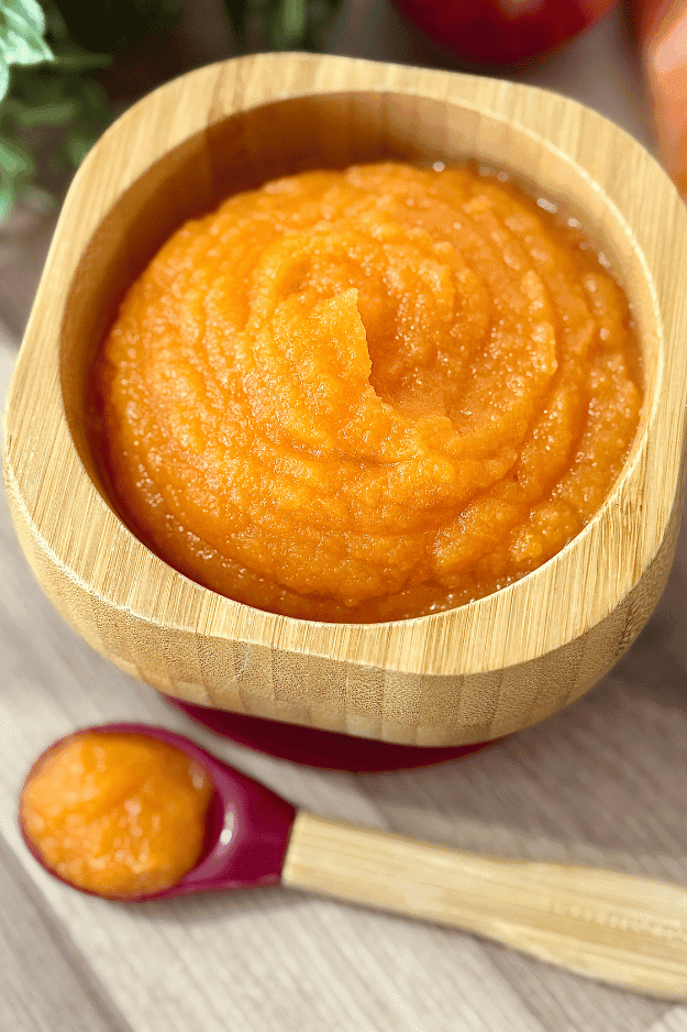 Smooth homemade apple carrot purée served in a wooden baby bowl with a matching spoon, perfect for baby food.