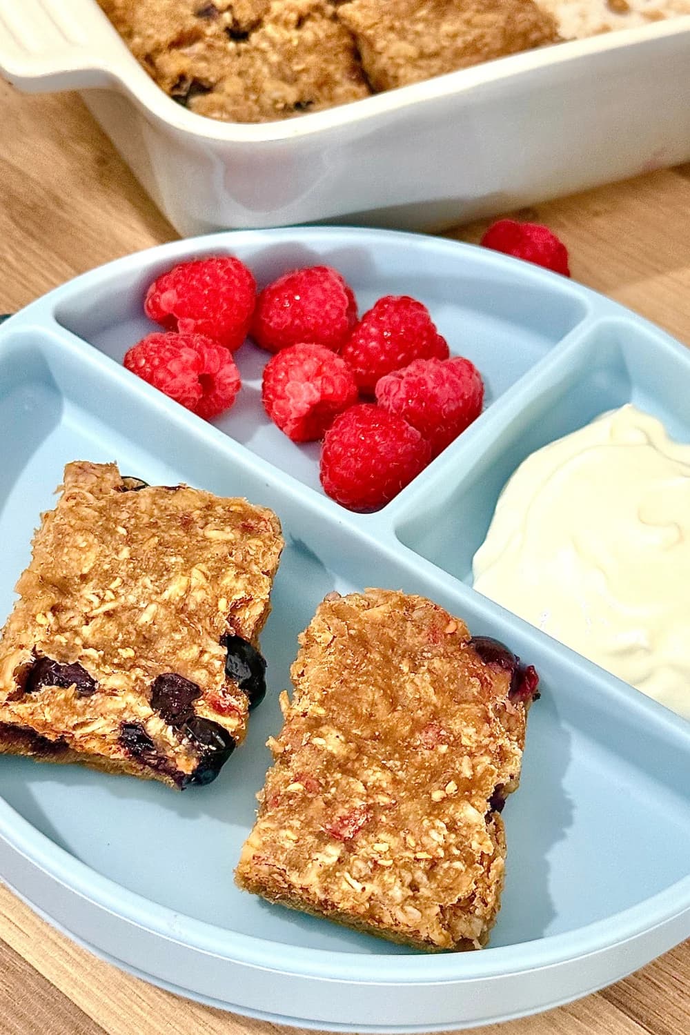 Protein berry oat bars served with fresh raspberries and Greek yogurt on a blue divided plate for a healthy breakfast or snack.