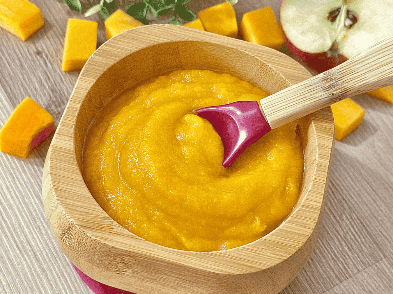Smooth squash and apple puree served in a wooden bowl with a baby spoon, surrounded by fresh squash cubes and apple slices.