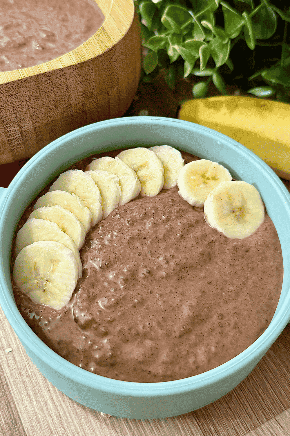"Creamy chocolate chia pudding topped with fresh banana slices in a blue bowl with bamboo spoon – healthy vegan breakfast or snack option