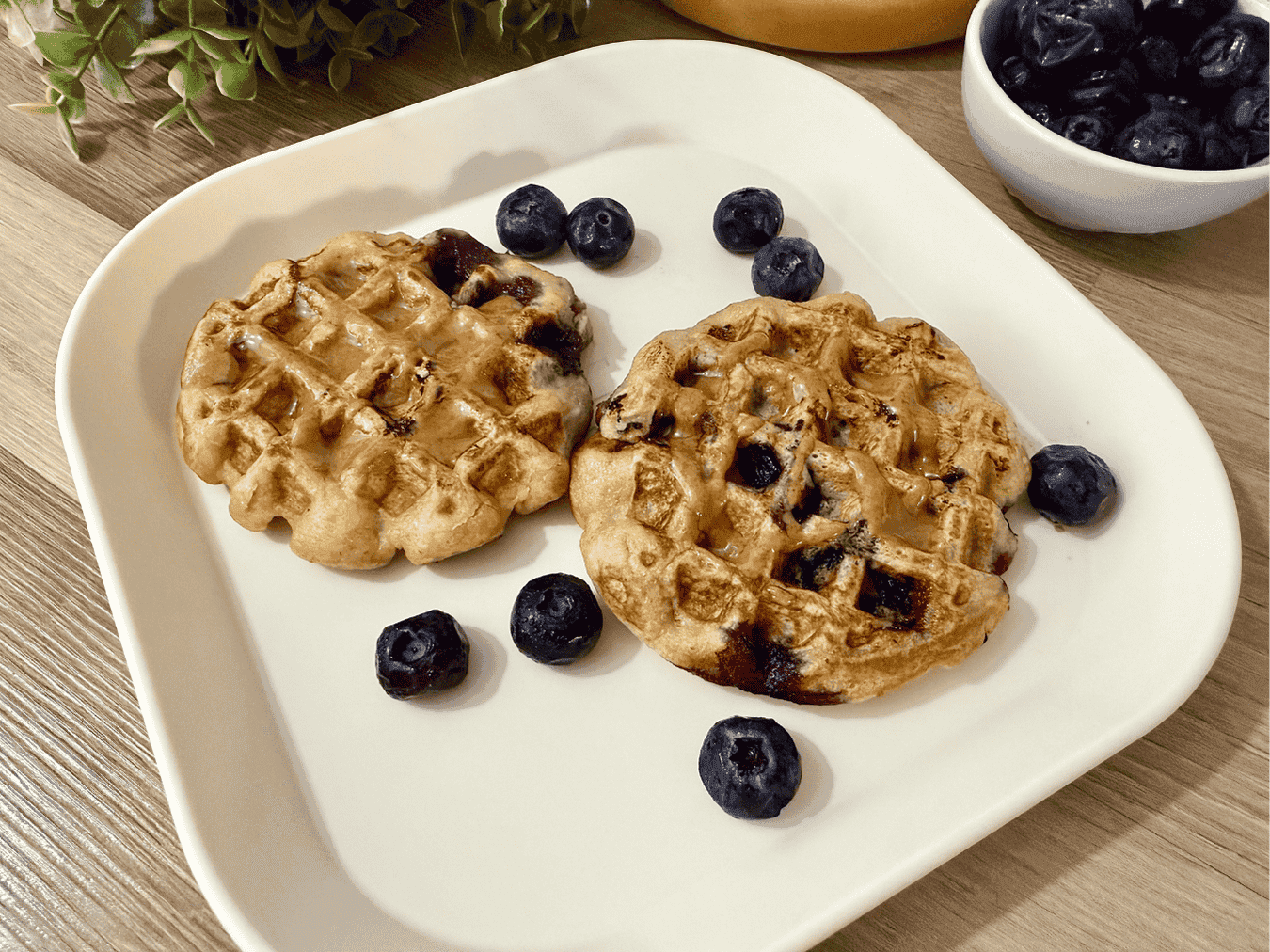 A stack of golden blueberry banana waffles topped with fresh blueberries and banana slices, drizzled with maple syrup. These soft and crispy waffles are made with ripe bananas and juicy blueberries, perfect for a nutritious and flavorful breakfast.