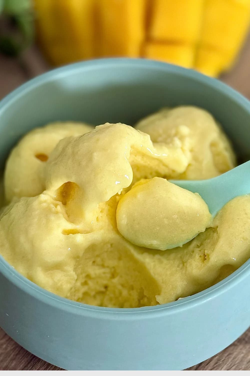 Close-up of vibrant yellow mango ice cream in a light blue bowl with a matching spoon.